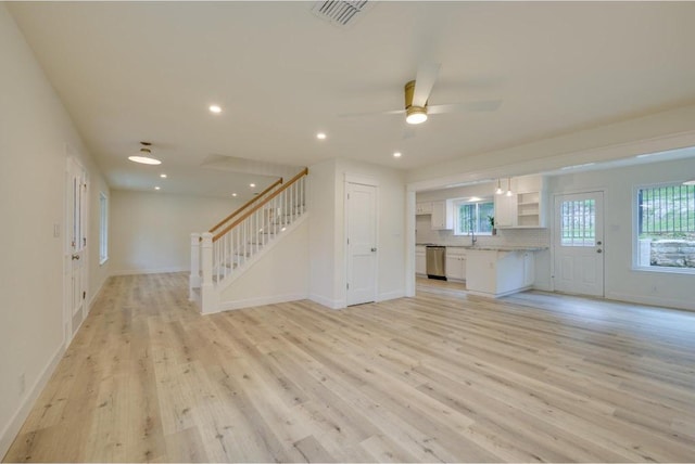 unfurnished living room featuring light wood-type flooring, visible vents, a ceiling fan, and stairway