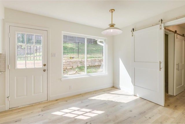 unfurnished dining area featuring a barn door, baseboards, and light wood finished floors