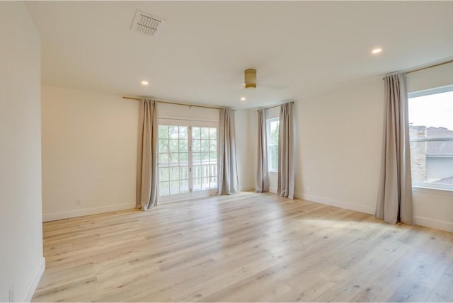 unfurnished room featuring light wood finished floors, visible vents, plenty of natural light, and baseboards