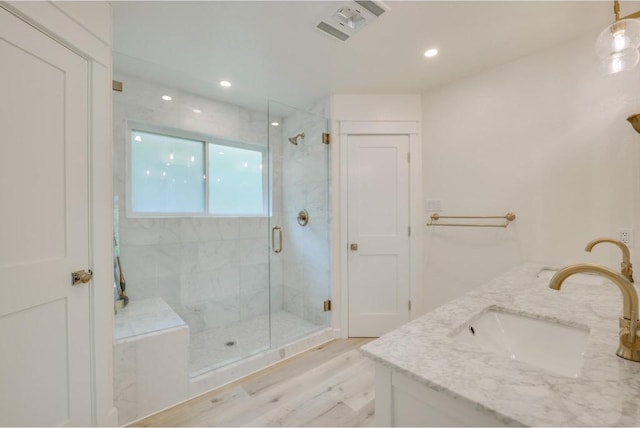 bathroom featuring a marble finish shower, visible vents, double vanity, wood finished floors, and a sink