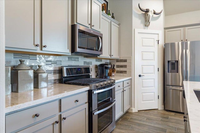 kitchen with light stone countertops, dark wood-style flooring, gray cabinetry, decorative backsplash, and appliances with stainless steel finishes