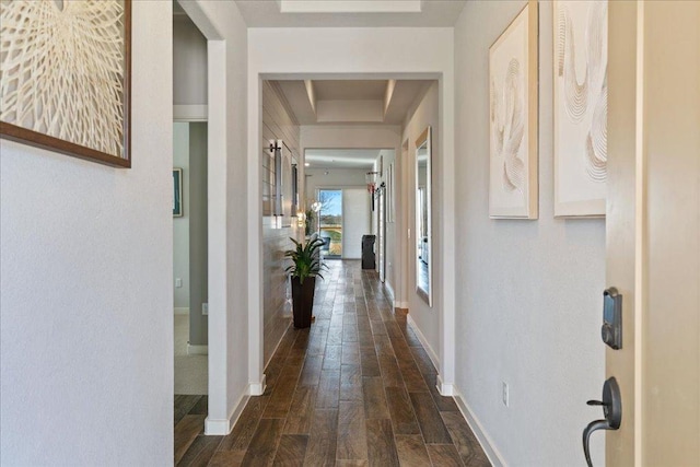 hallway featuring a raised ceiling, baseboards, and wood tiled floor