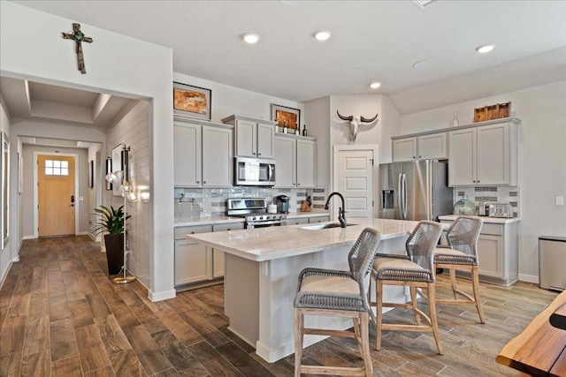7708 Skytree Dr, Austin, TX 78744 - kitchen with stainless steel appliances, a kitchen bar, dark wood-type flooring, tasteful backsplash, and an island with sink