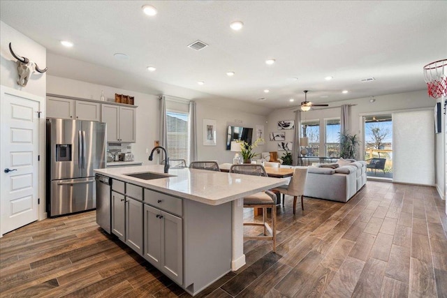 kitchen featuring visible vents, gray cabinetry, a sink, appliances with stainless steel finishes, and a kitchen breakfast bar