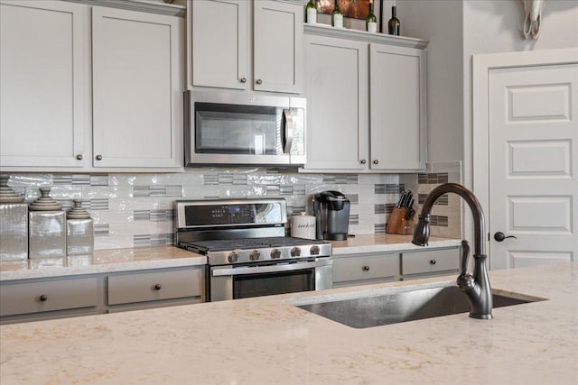 kitchen with tasteful backsplash, light stone counters, gray cabinets, appliances with stainless steel finishes, and a sink