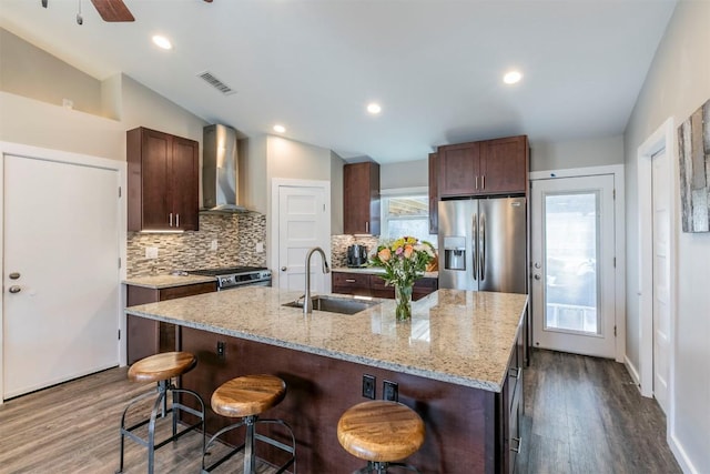 kitchen with a breakfast bar area, visible vents, stainless steel appliances, a sink, and wall chimney exhaust hood