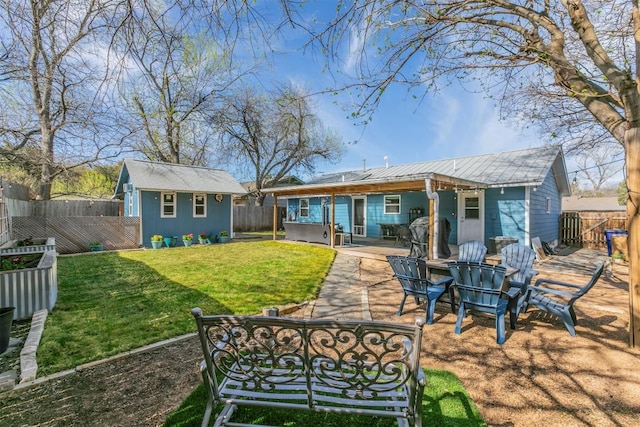 rear view of property with metal roof, a yard, an outdoor structure, a fenced backyard, and a patio