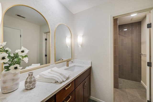 bathroom with vanity, visible vents, tiled shower, tile patterned floors, and a textured wall