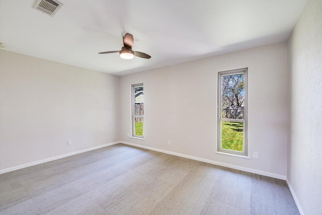 carpeted empty room with baseboards, visible vents, a wealth of natural light, and ceiling fan