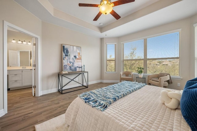 bedroom featuring wood finished floors, baseboards, a tray ceiling, ceiling fan, and a sink