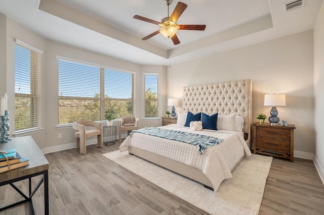 bedroom featuring visible vents, a raised ceiling, baseboards, and wood finished floors