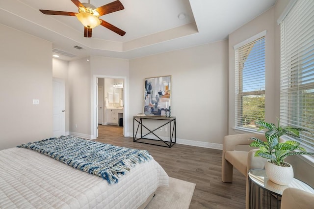 bedroom featuring a tray ceiling, baseboards, visible vents, and wood finished floors