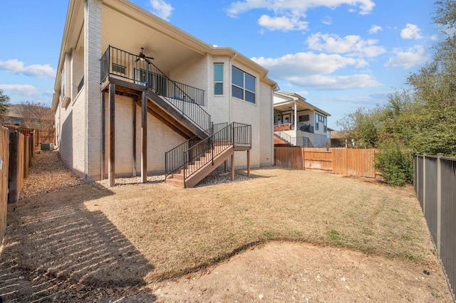 rear view of property featuring stucco siding, a ceiling fan, stairs, and a fenced backyard