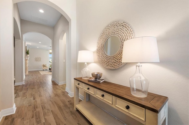 hallway featuring recessed lighting, wood finished floors, arched walkways, and baseboards