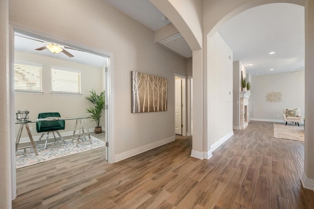 hall with baseboards, arched walkways, and wood finished floors