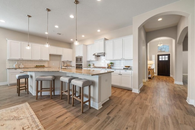 kitchen featuring arched walkways, light wood-style floors, under cabinet range hood, appliances with stainless steel finishes, and white cabinetry