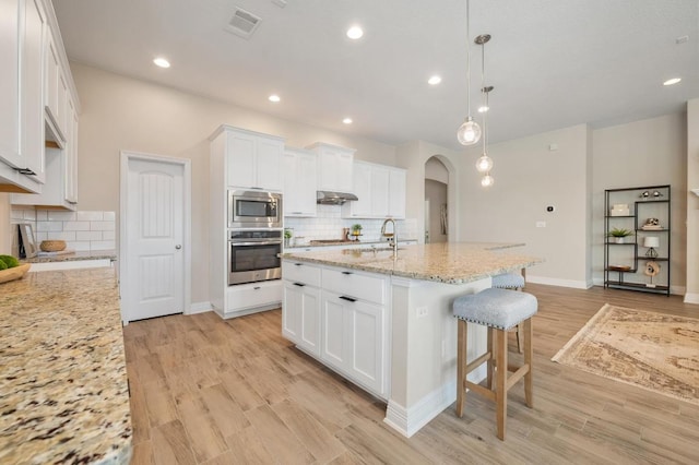 kitchen with arched walkways, white cabinetry, stainless steel appliances, and light wood-type flooring