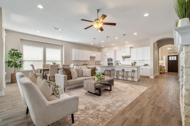 living room with light wood finished floors, visible vents, recessed lighting, arched walkways, and a ceiling fan