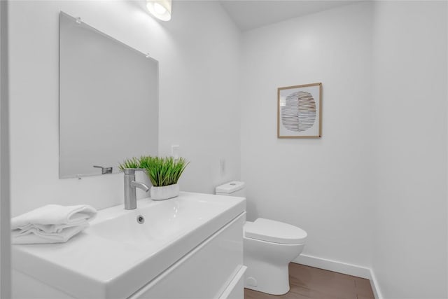 half bathroom featuring baseboards, toilet, wood finished floors, and vanity