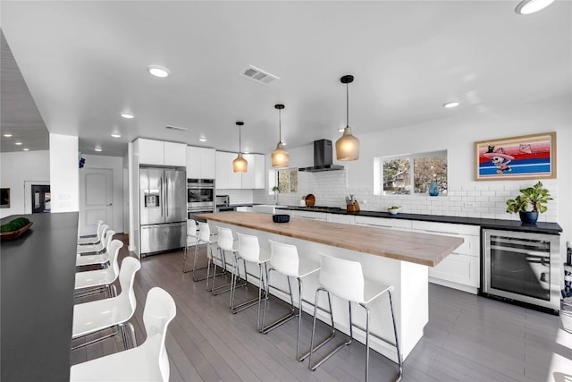 kitchen featuring visible vents, wine cooler, appliances with stainless steel finishes, wood counters, and wall chimney range hood