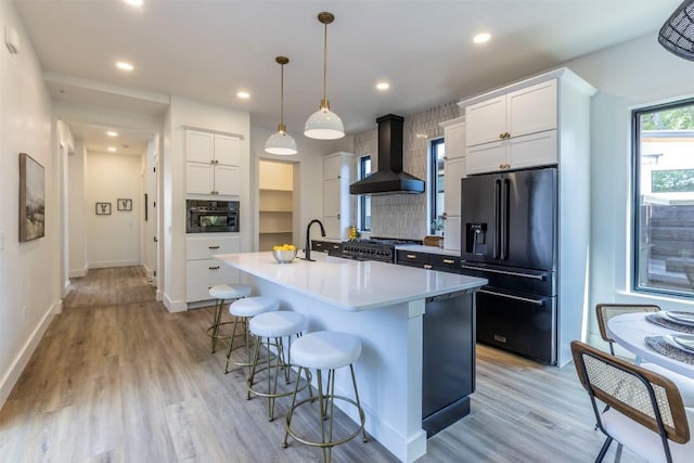 kitchen featuring ventilation hood, black appliances, light wood-style floors, a kitchen breakfast bar, and tasteful backsplash