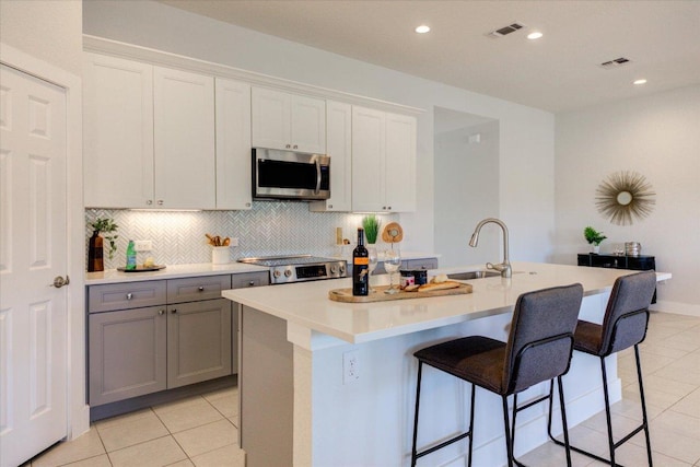 kitchen featuring visible vents, backsplash, an island with sink, appliances with stainless steel finishes, and light tile patterned flooring