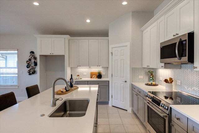 kitchen featuring light countertops, light tile patterned floors, decorative backsplash, stainless steel appliances, and a sink