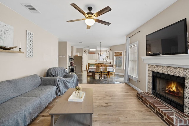 living room with a tile fireplace, ceiling fan with notable chandelier, visible vents, and light wood-type flooring