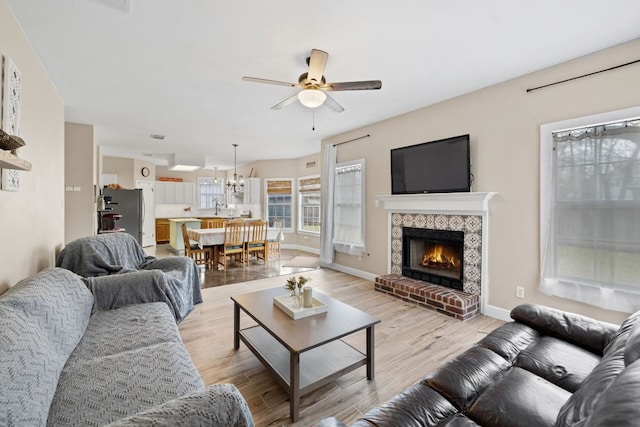 living room with light wood-type flooring, baseboards, a brick fireplace, and ceiling fan