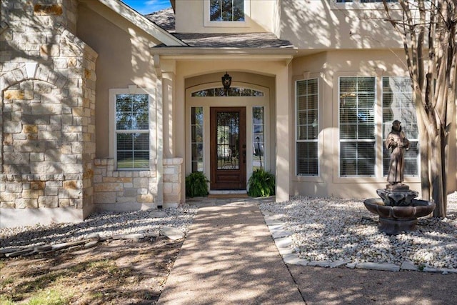 view of exterior entry featuring stucco siding, stone siding, and a shingled roof