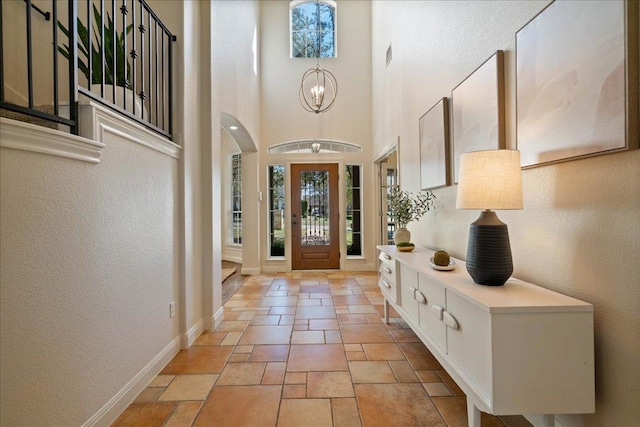 entrance foyer with stone tile floors, baseboards, an inviting chandelier, a towering ceiling, and a textured wall