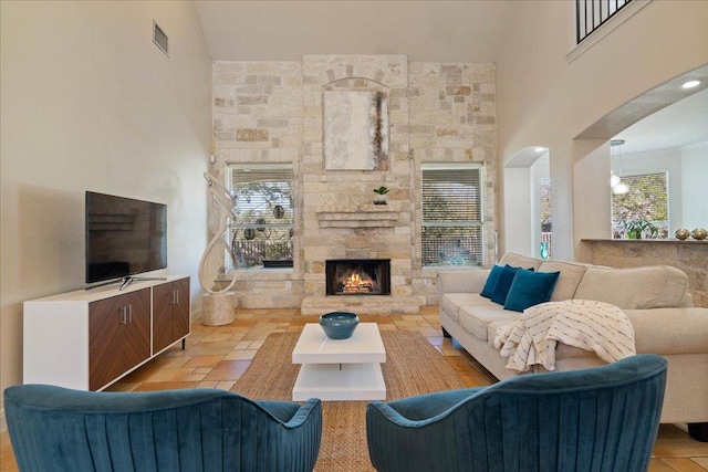 living area featuring a stone fireplace, a healthy amount of sunlight, and a towering ceiling