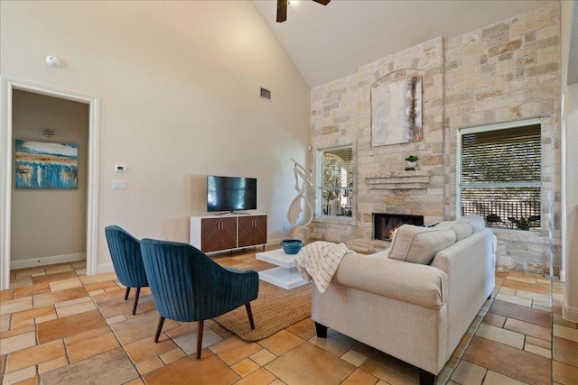 living room featuring a ceiling fan, baseboards, visible vents, high vaulted ceiling, and a stone fireplace