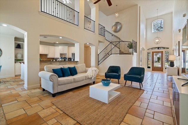 living room featuring stone tile floors, arched walkways, baseboards, and ceiling fan