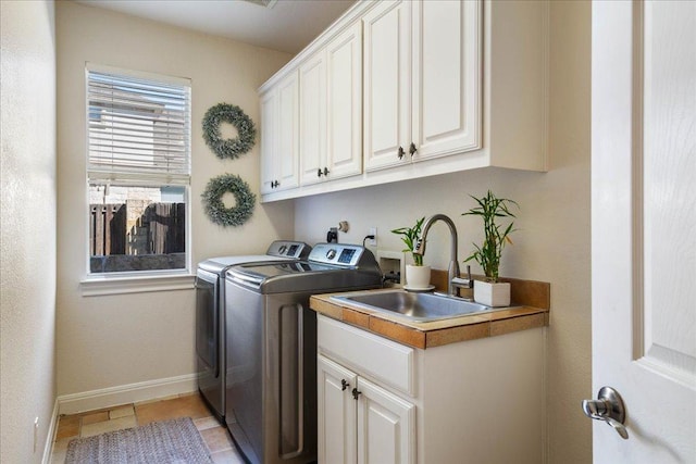 washroom featuring baseboards, light tile patterned floors, cabinet space, independent washer and dryer, and a sink