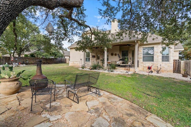 rear view of property featuring fence, a chimney, stone siding, a patio area, and a lawn