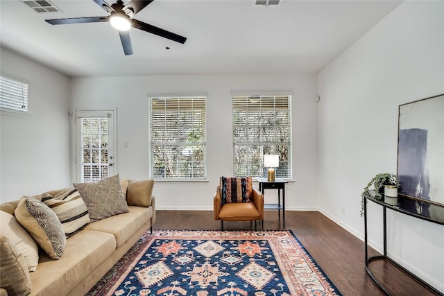 living room featuring visible vents, baseboards, dark wood-type flooring, and ceiling fan