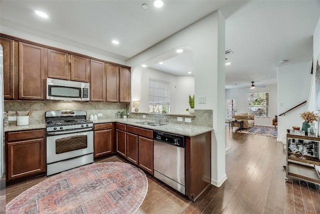 kitchen with a sink, light stone counters, backsplash, wood-type flooring, and appliances with stainless steel finishes