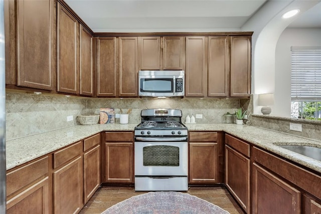 kitchen with light stone countertops, arched walkways, a sink, decorative backsplash, and appliances with stainless steel finishes