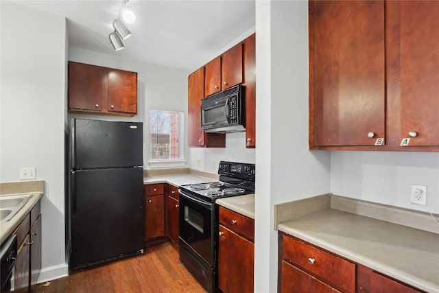 kitchen with black appliances, a sink, wood finished floors, light countertops, and dark brown cabinets