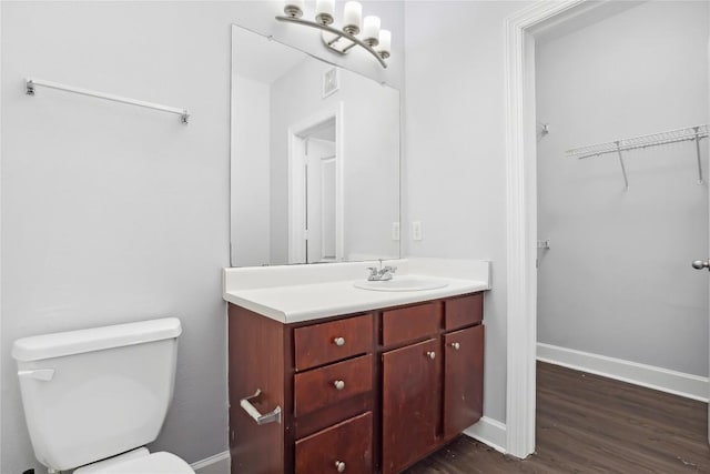 bathroom featuring toilet, wood finished floors, vanity, baseboards, and a spacious closet