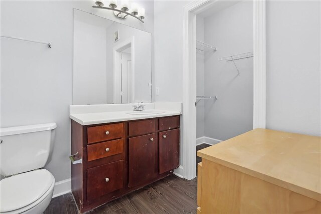 bathroom with a spacious closet, baseboards, toilet, wood finished floors, and vanity