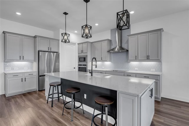 kitchen with wall chimney range hood, gray cabinets, dark wood-style floors, stainless steel appliances, and a sink