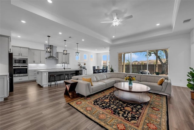 living room with visible vents, ceiling fan, a tray ceiling, and wood finished floors