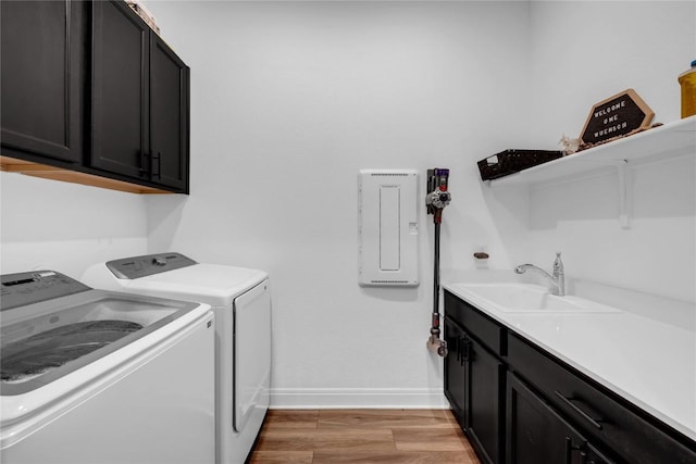 laundry area featuring baseboards, washing machine and dryer, light wood-type flooring, cabinet space, and a sink