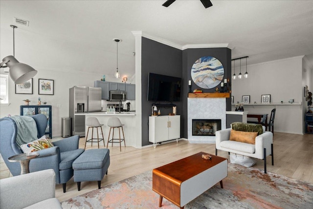 living room with a ceiling fan, visible vents, light wood-type flooring, and ornamental molding