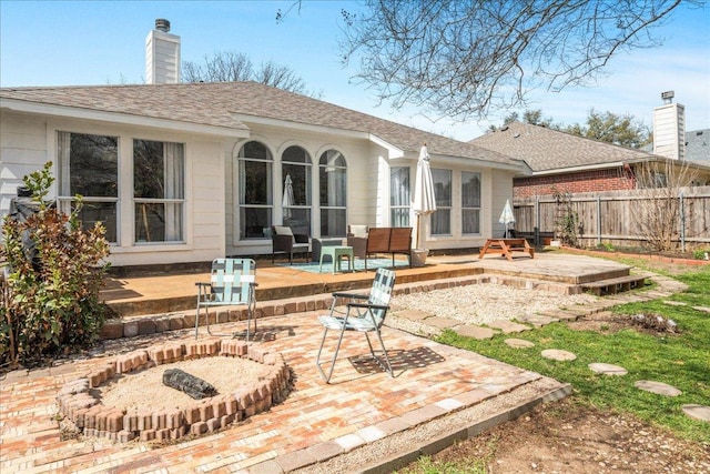 rear view of property featuring a shingled roof, a patio area, fence, and a chimney