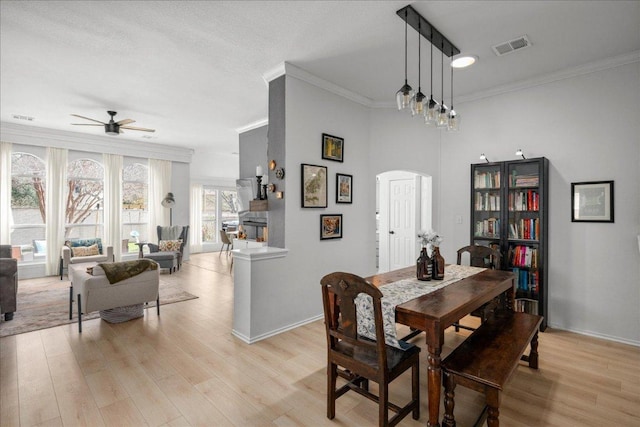 dining space with visible vents, crown molding, ceiling fan, light wood-style floors, and arched walkways