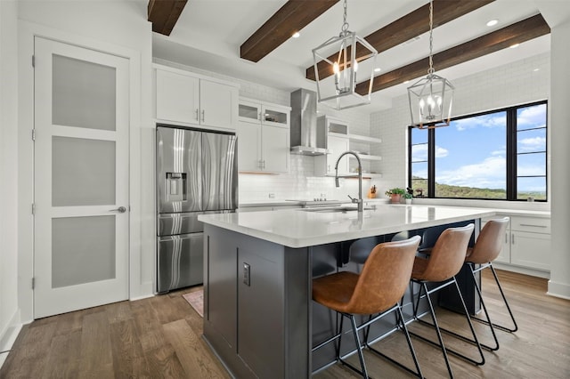 kitchen with wood finished floors, light countertops, stainless steel refrigerator with ice dispenser, wall chimney exhaust hood, and a chandelier