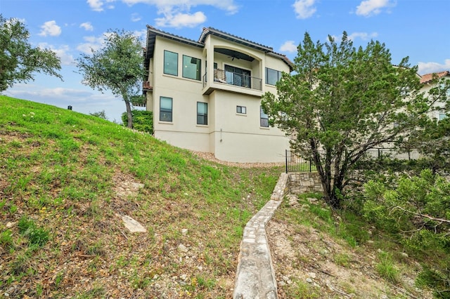 back of house with a balcony, fence, and stucco siding